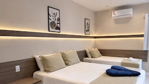 Habitación de hotel con dos camas, un aire acondicionado de pared y dos cuadros enmarcados.