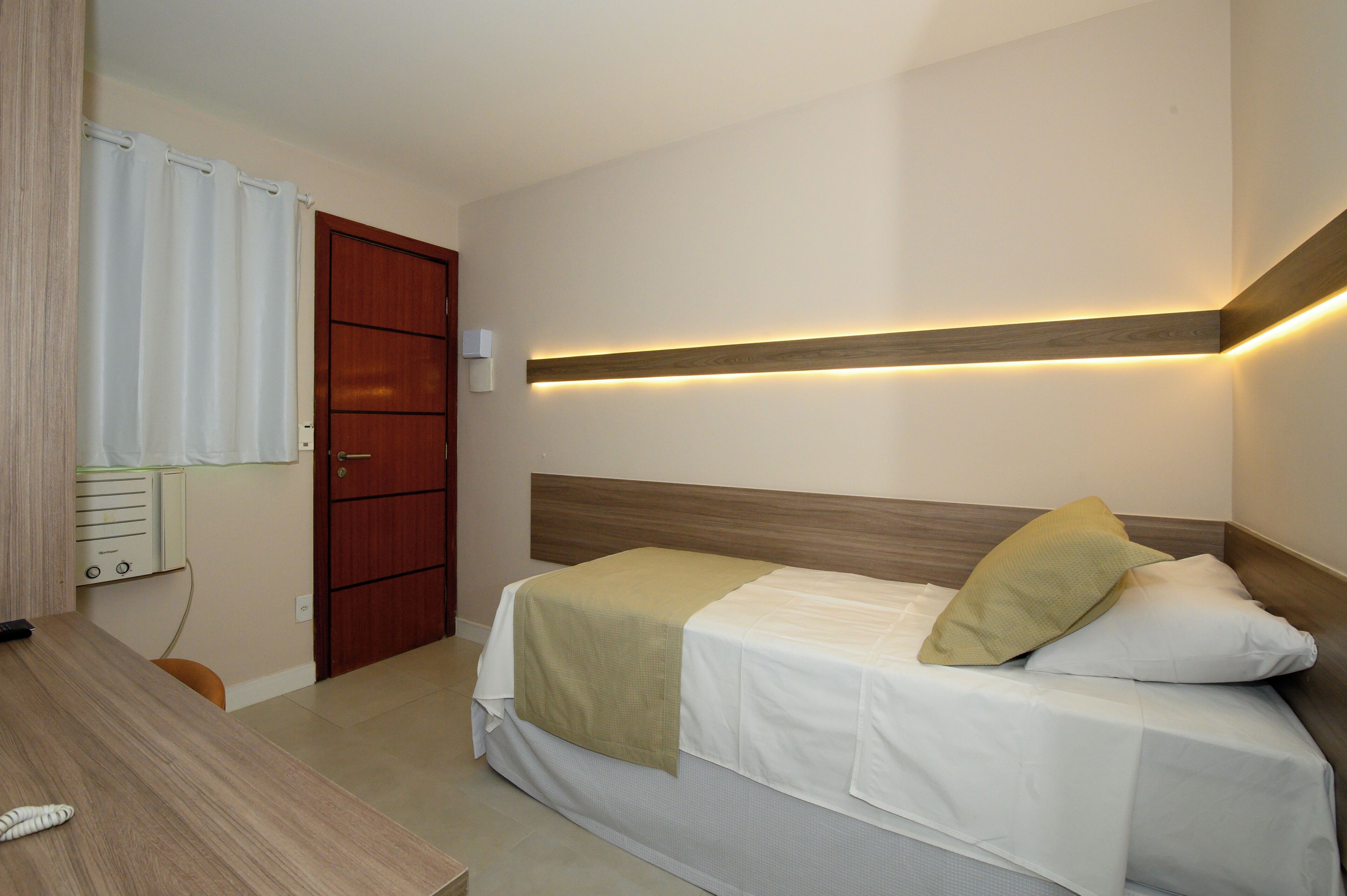 A single bed with a wooden headboard, a bedside table, and a wall-mounted light fixture.