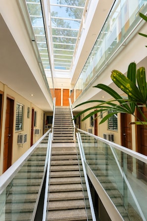 Un intérieur moderne avec un escalier central, des rampes en verre et une vue sur l’extérieur grâce à des fenêtres de toit.