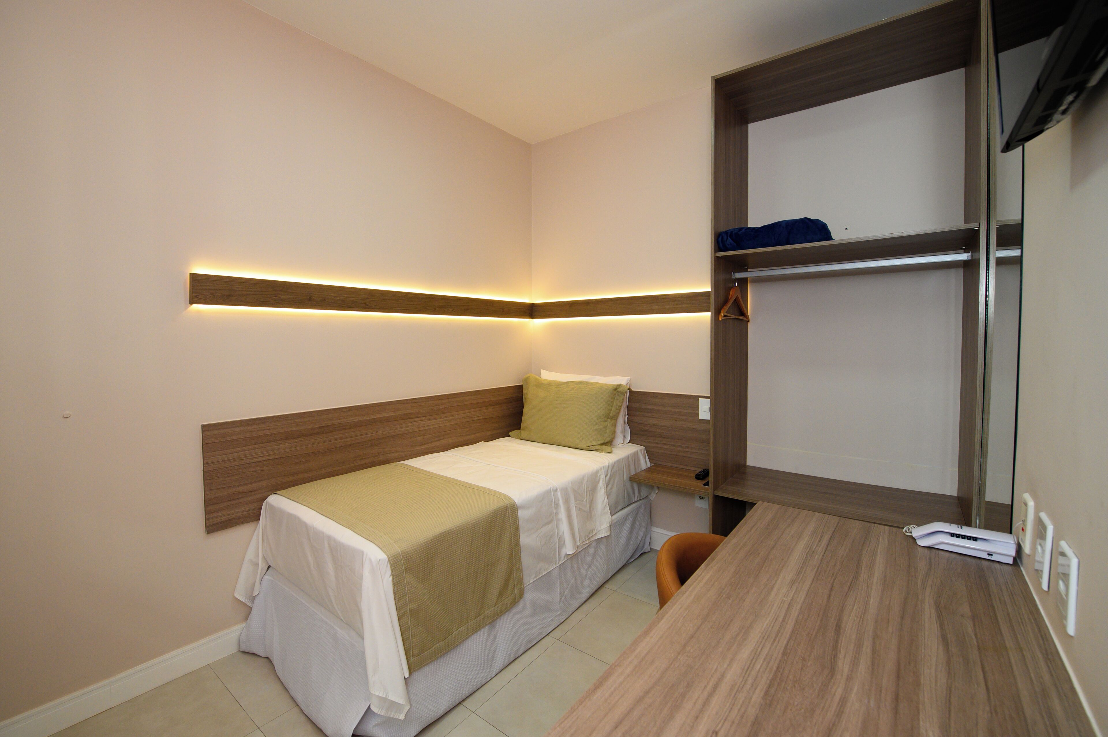 Una habitación de hotel pequeña con una cama individual, un escritorio y un armario empotrado.