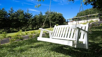 A white swing bench in a grassy park area with trees and a road in the background.