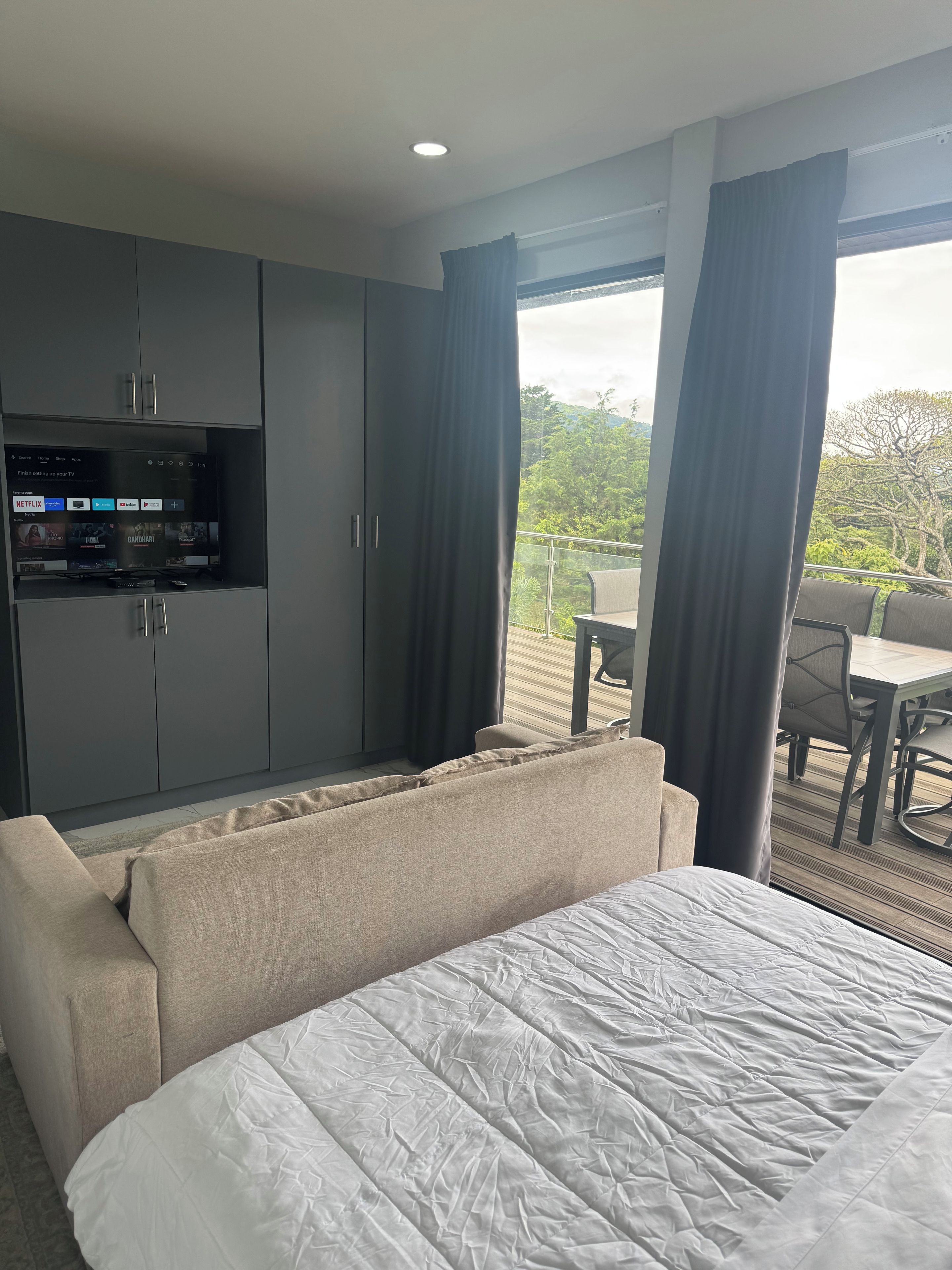 Une chambre d’hôtel comprenant un lit, un canapé, une télévision et un balcon avec une table et des chaises.