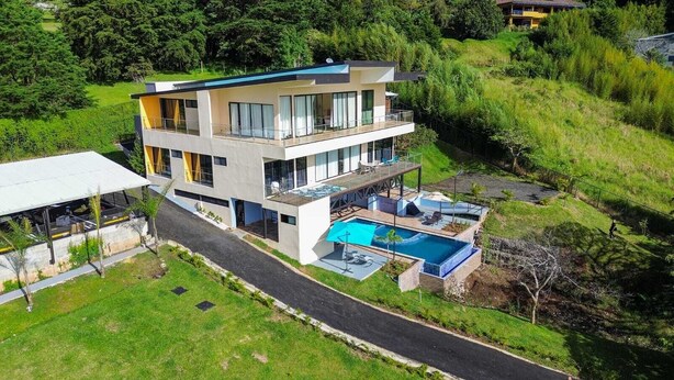 Una casa moderna de varios pisos con un balcón grande, piscina y césped bien cuidado.