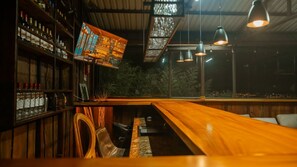 A bar area with wooden shelves stocked with bottles, a long wooden counter, and hanging pendant lights.