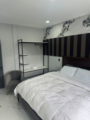 A modern bedroom with a large bed, a built-in wardrobe, a chair, and a marble-patterned wall.