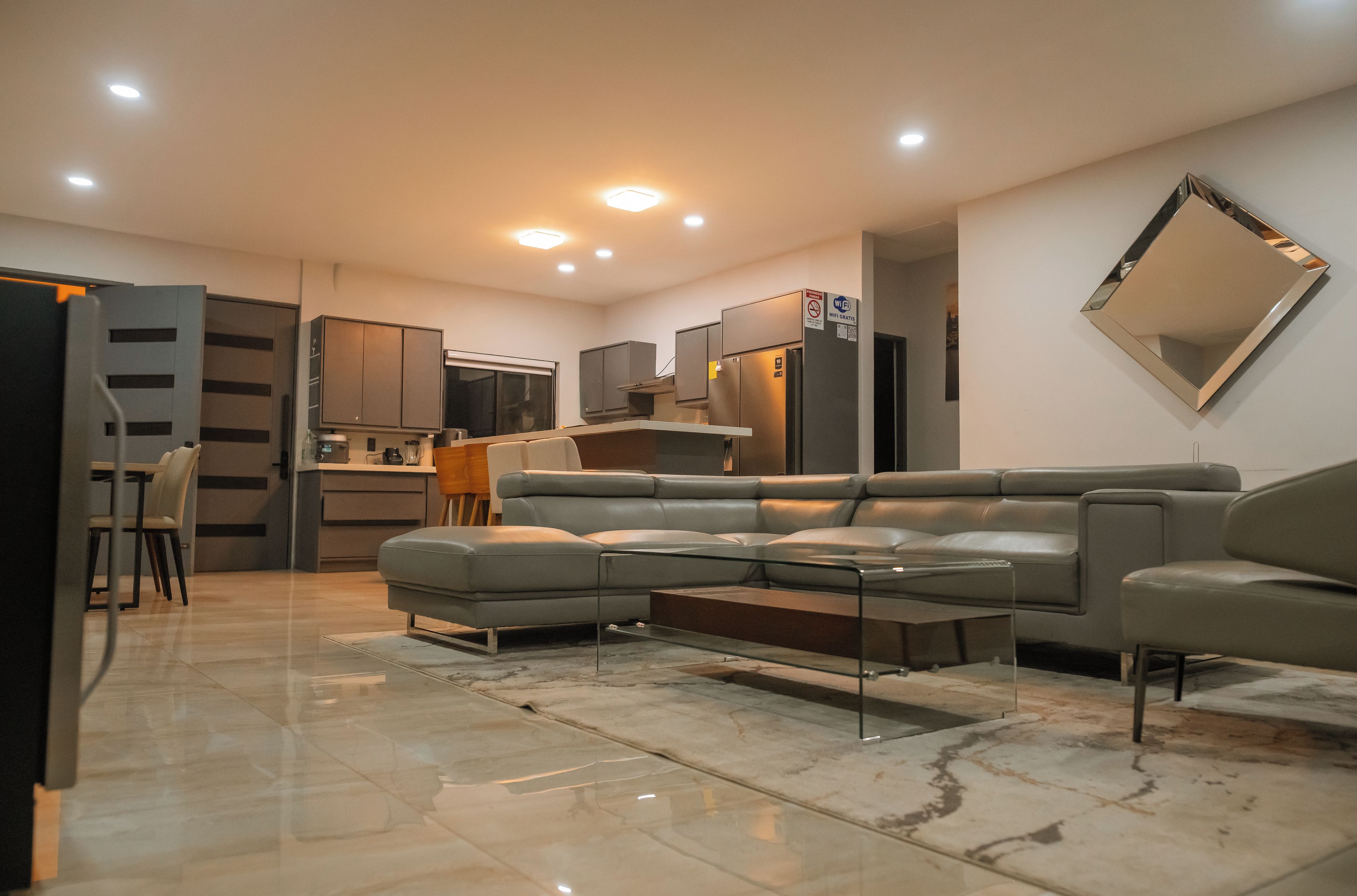 Een moderne woonkamer met een hoekbank, een eethoek met een tafel en stoelen, en een keuken met kasten en een koelkast.