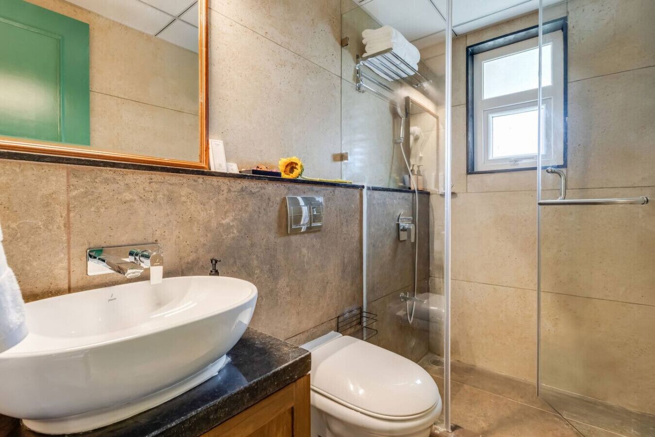 Un baño moderno con un lavabo grande de color blanco, un inodoro, una ducha con cerramiento de vidrio y un espejo sobre el lavabo.