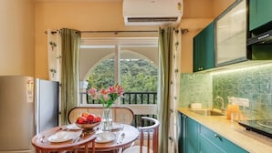 A kitchen with a dining area, a view of greenery, and a window with curtains. - 1BR in North Goa Pool Gym Clubhouse Access (Mapusa)