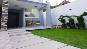 Una casa moderna con un pilar de piedra, una escalera de cristal y un césped bien cuidado.