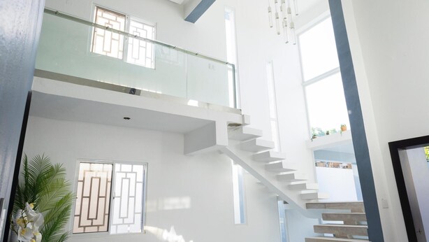 Un interior amplio y moderno con techo alto, una escalera que lleva a un nivel superior y un gran ventanal que deja entrar luz natural.