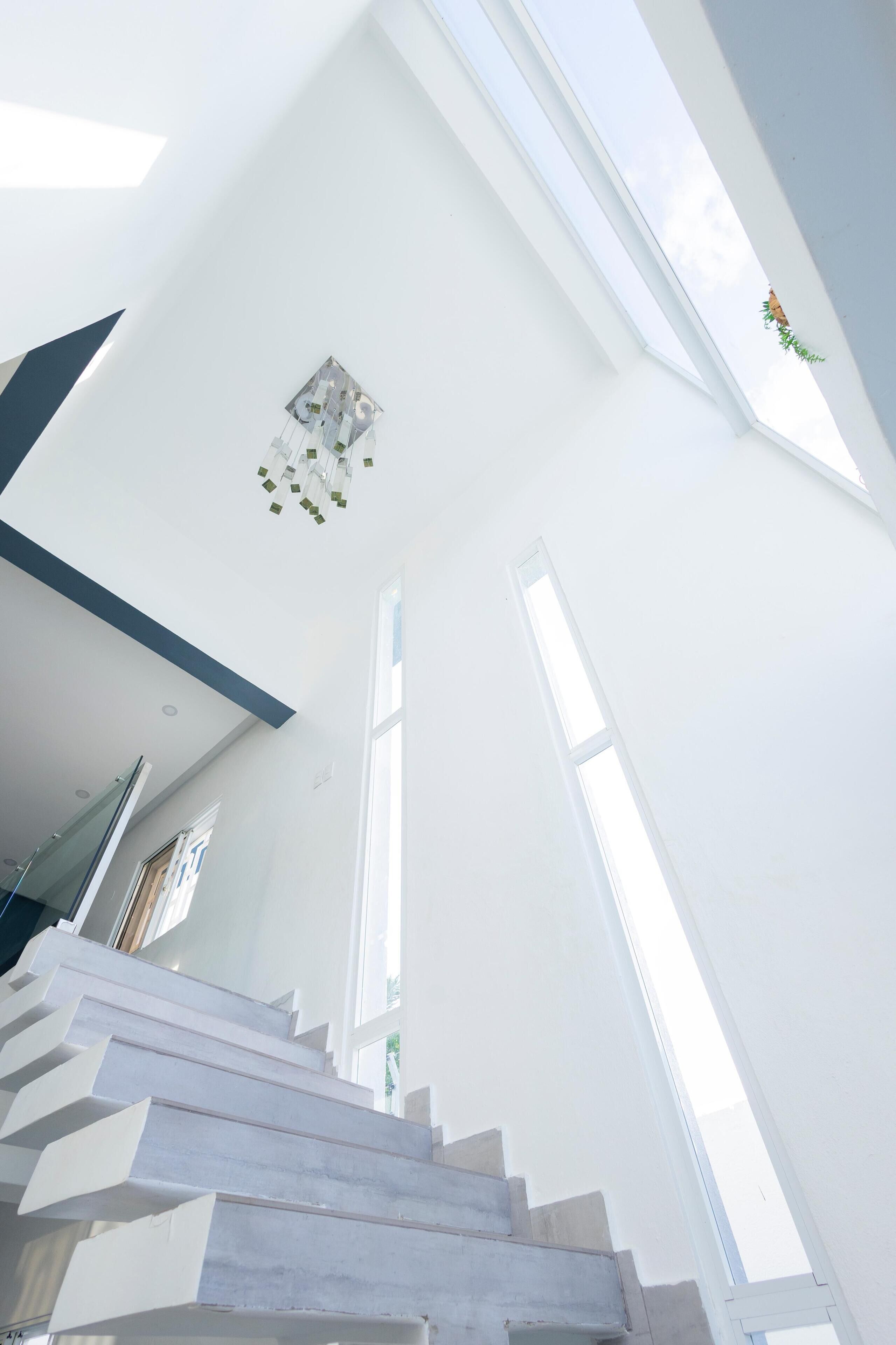 A modern interior with a staircase leading upwards, large windows allowing natural light, and a minimalist design.
