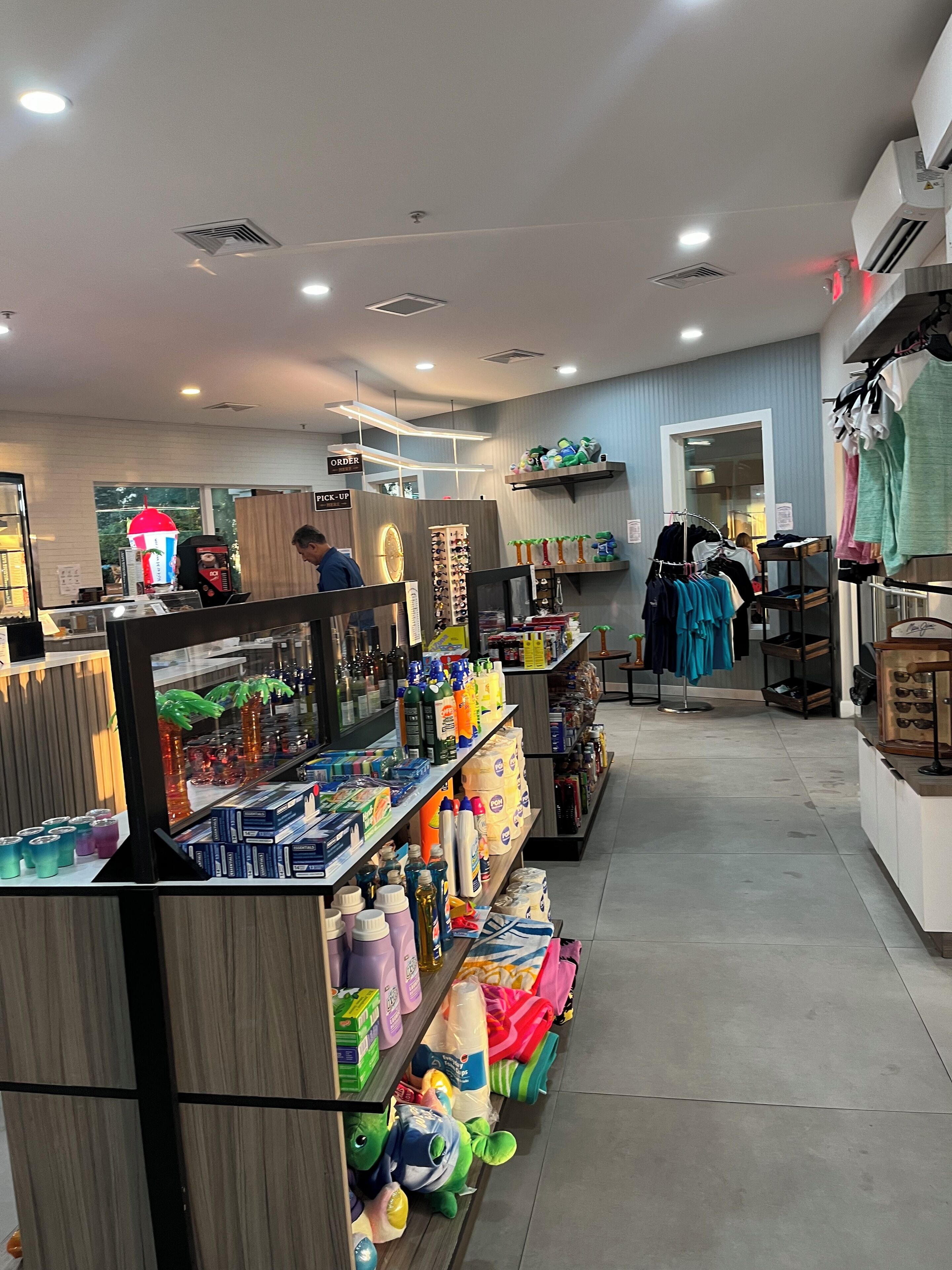 A well-lit retail store with shelves stocked with various products, a customer service counter, and a clothing rack.