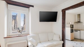 A white sofa, a TV, a window with a view, a kitchen area, and a chair. - House for 9 People, Cancale Port (Cancale)