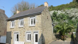 A stone building with multiple windows and a sloped roof, surrounded by greenery and a clear sky. - House for 9 People, Cancale Port (Cancale)