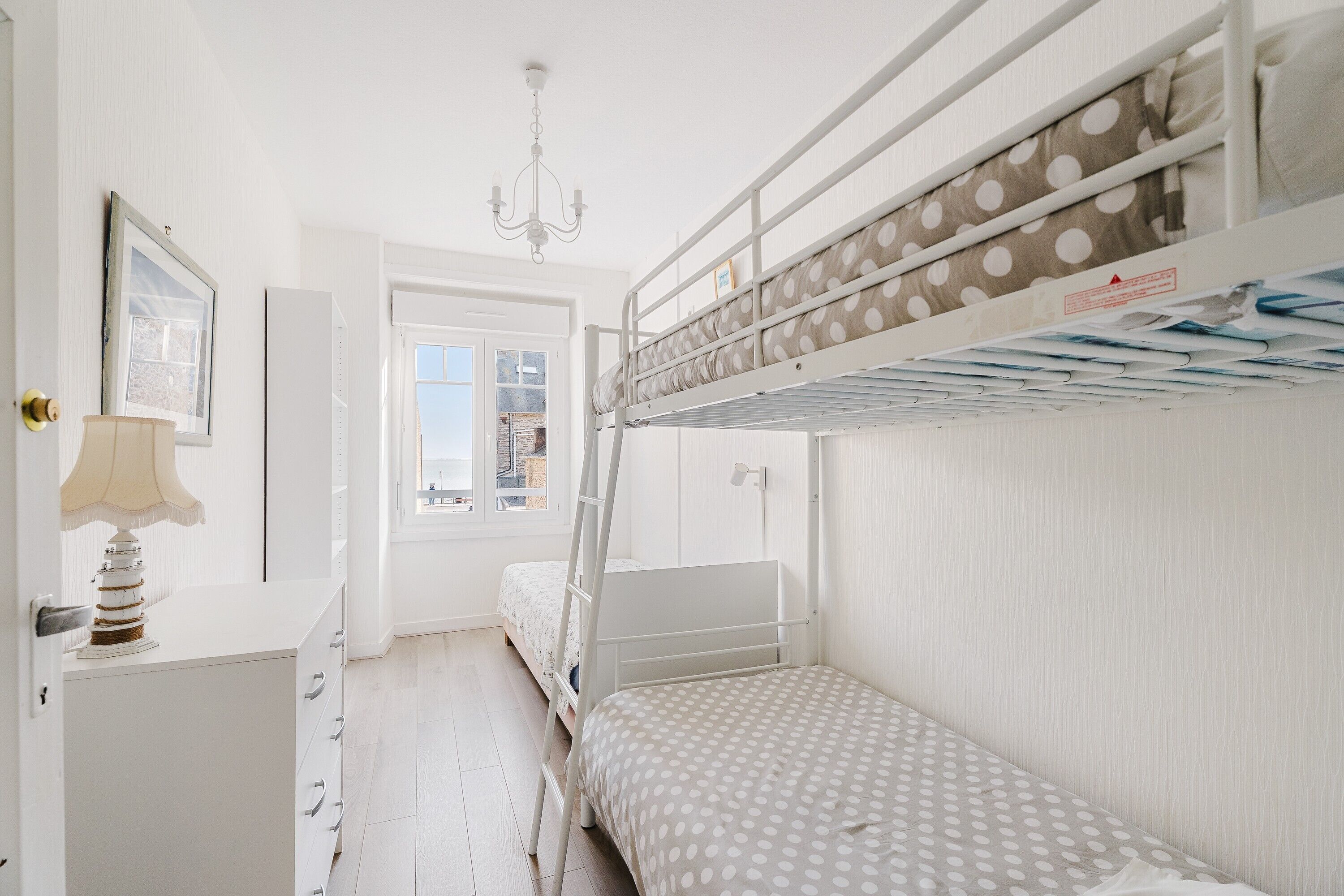 Une chambre avec un lit superposé, une échelle, un bureau avec une lampe et une fenêtre donnant sur un beau paysage.