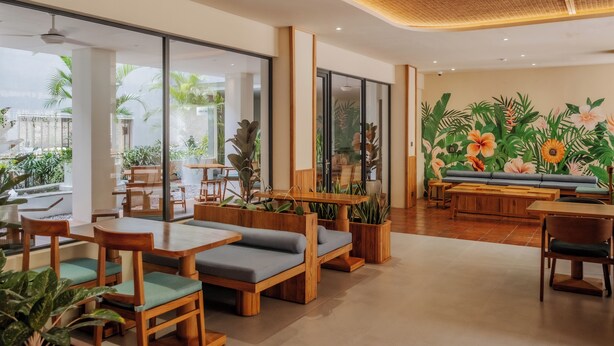 Un café moderno con mobiliario de madera, ventanas amplias y arte mural tropical.
