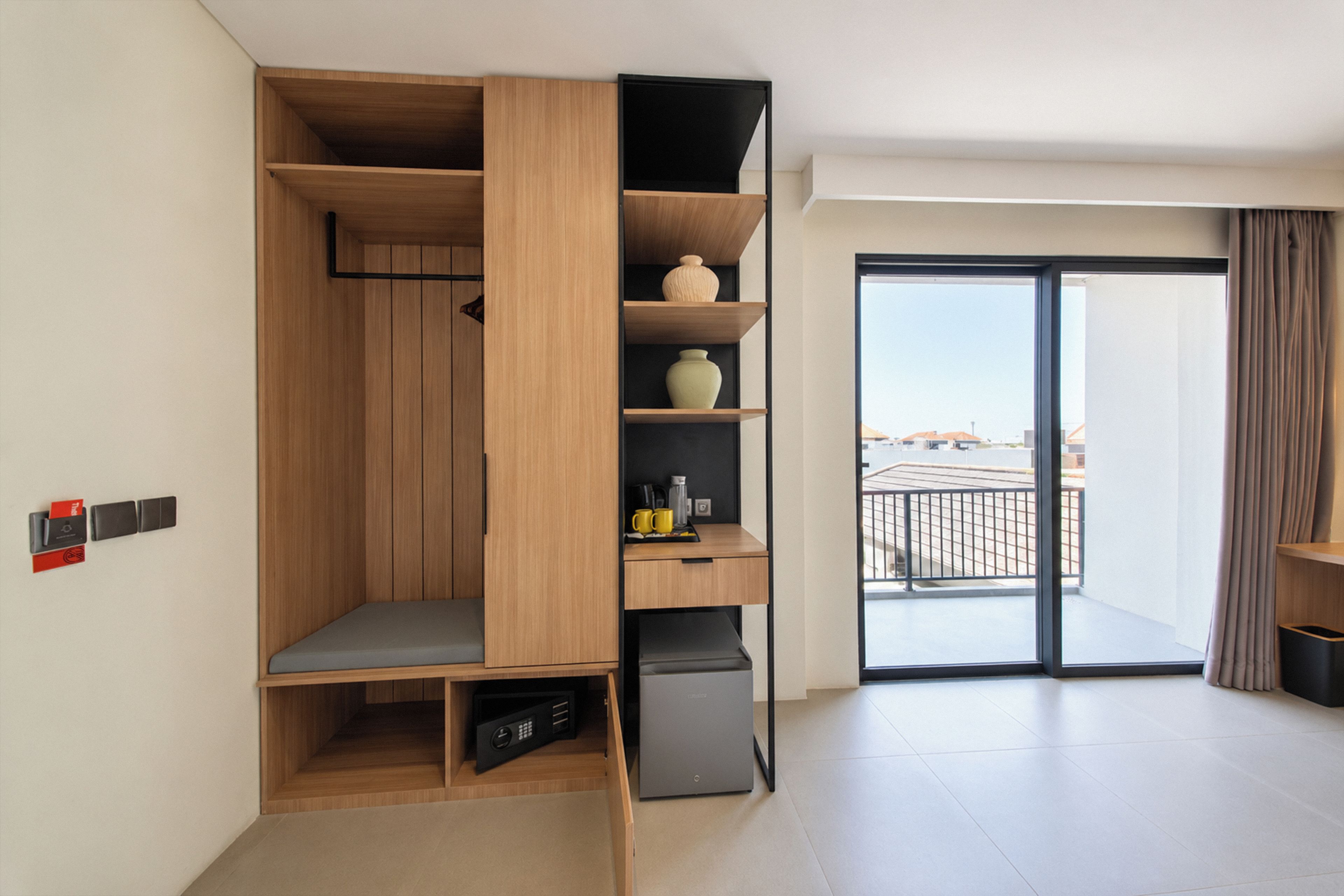 A modern room with a built-in wardrobe, a small seating area, a coffee machine, and a view of the outside through a large sliding door.