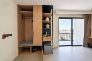 A modern room with a built-in wardrobe, a small seating area, a coffee machine, and a view of the outside through a large sliding door. - TheNomad Canggu (Canggu)