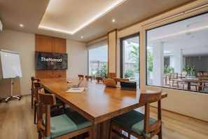 A conference room with a long wooden table, multiple chairs, a whiteboard, and a large window offering a view of the outdoors. - TheNomad Canggu (Canggu)