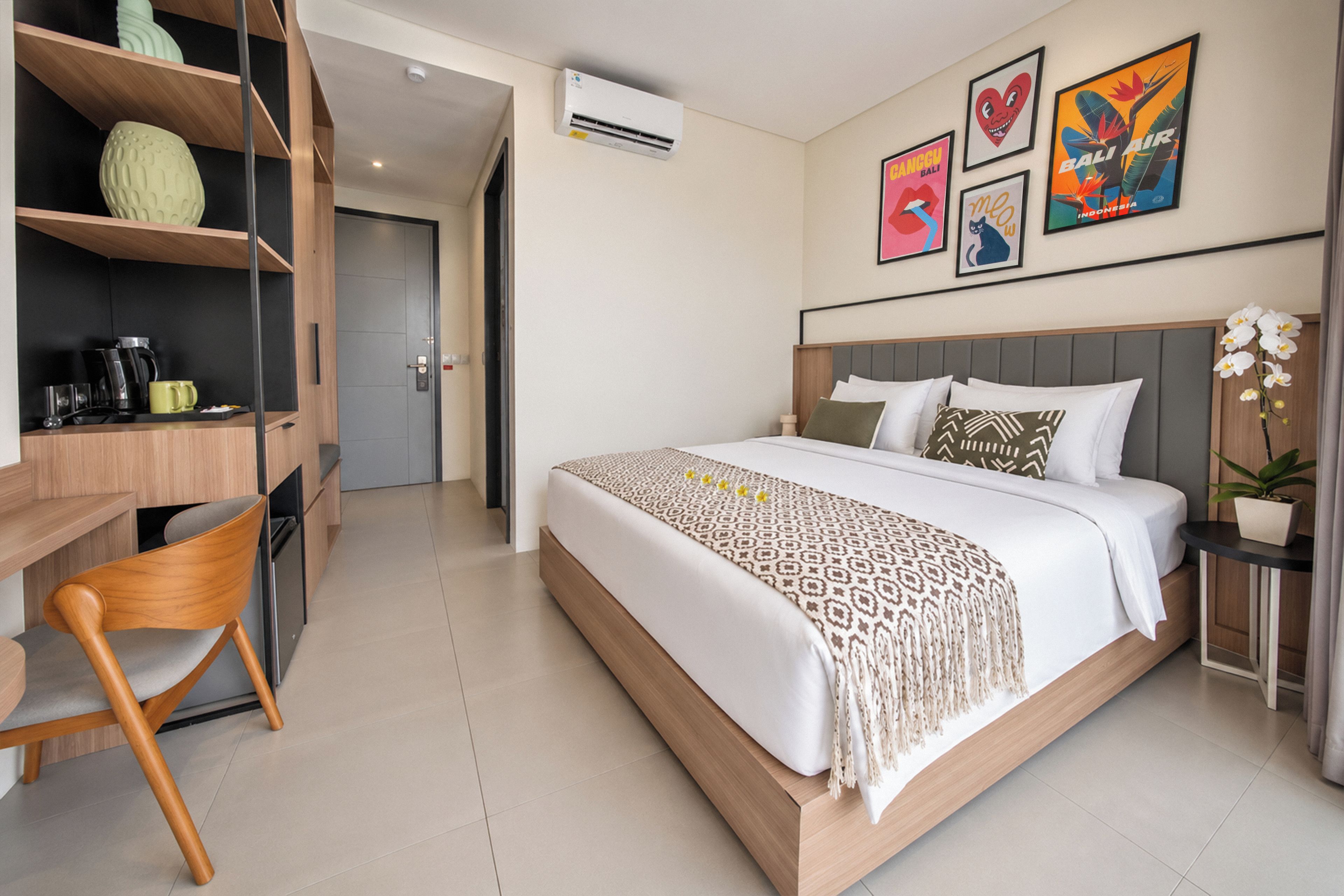 Habitación de hotel con cama, escritorio y silla. Incluye obras de arte en las paredes y una planta en maceta.