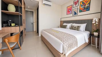 Habitación de hotel con cama, escritorio y silla. Incluye obras de arte en las paredes y una planta en maceta.