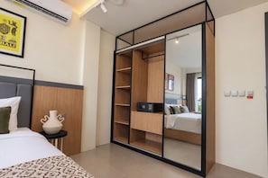 A hotel room with a bed, a bedside table with a vase, a wardrobe with a mirror, and a view of another room. - TheNomad Canggu (Canggu)
