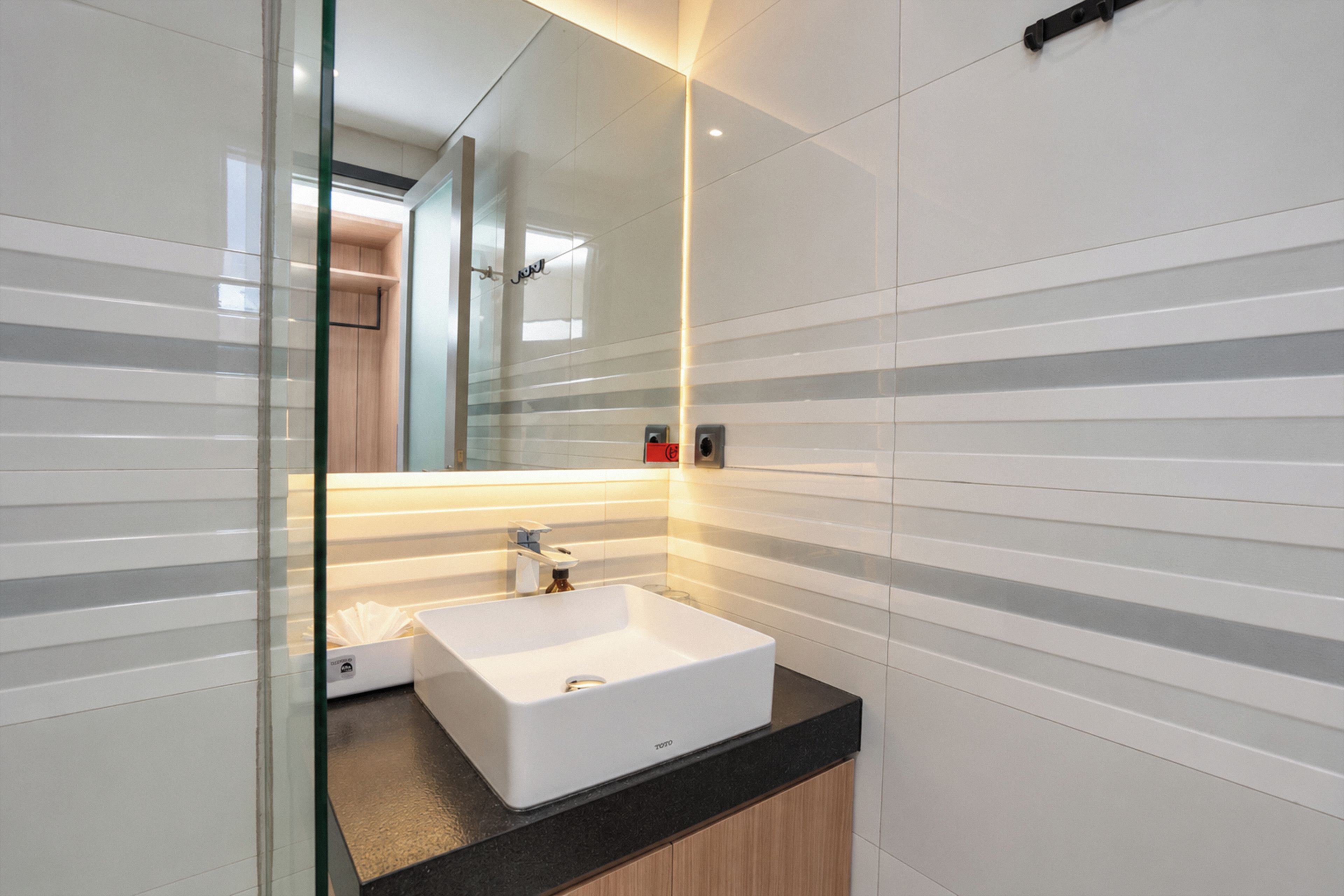 A modern bathroom with a white sink, a mirror, and striped wall tiles.