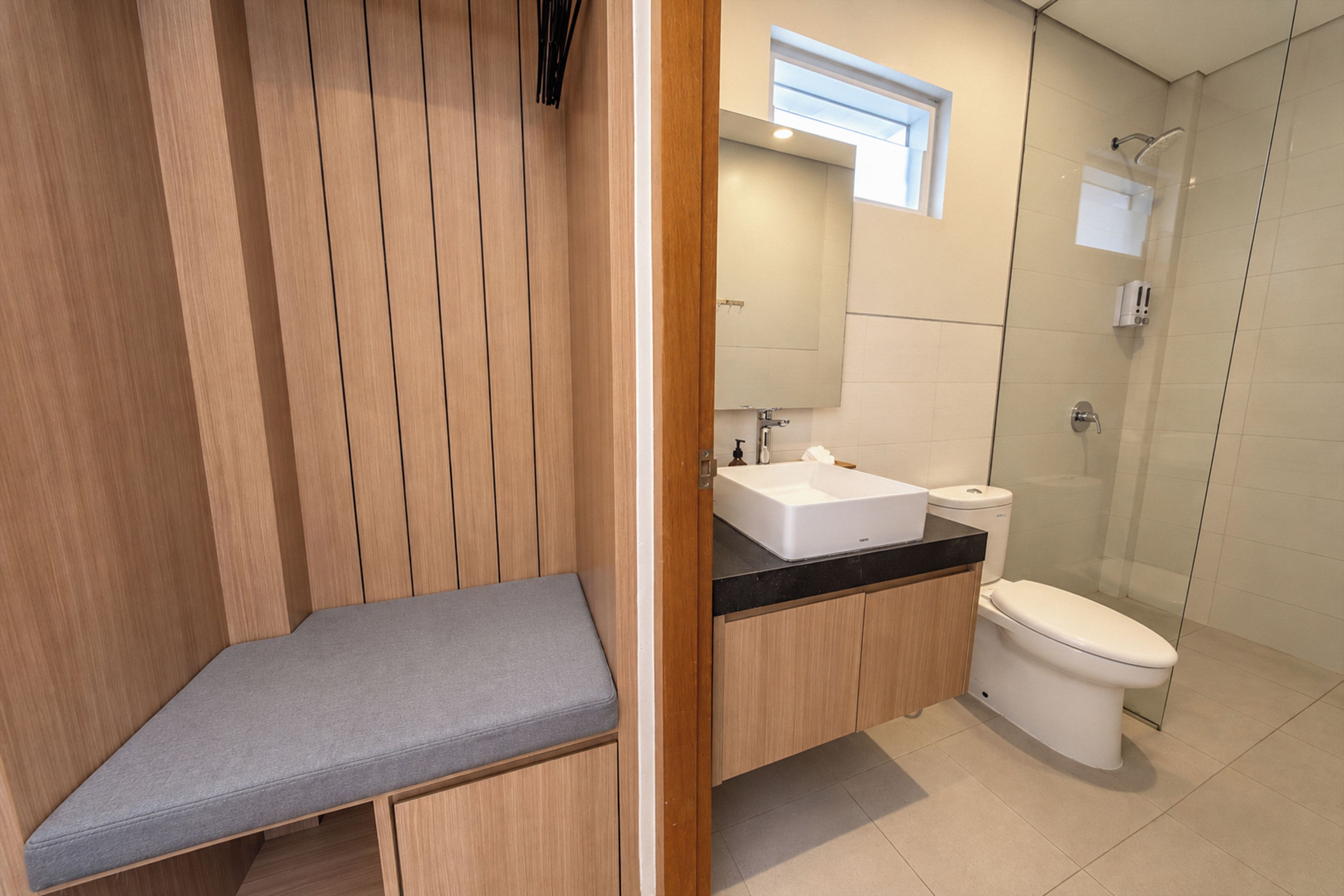 A modern bathroom with a wooden vanity, a bench, a sink, and a toilet.