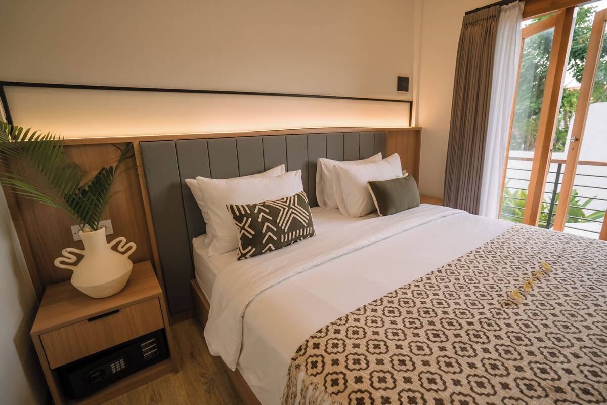 A hotel room with a bed, bedside table, and a nightstand with a plant.