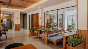 Un interior de restaurante moderno con mobiliario de madera, asientos acolchados color verde y plantas en macetas.