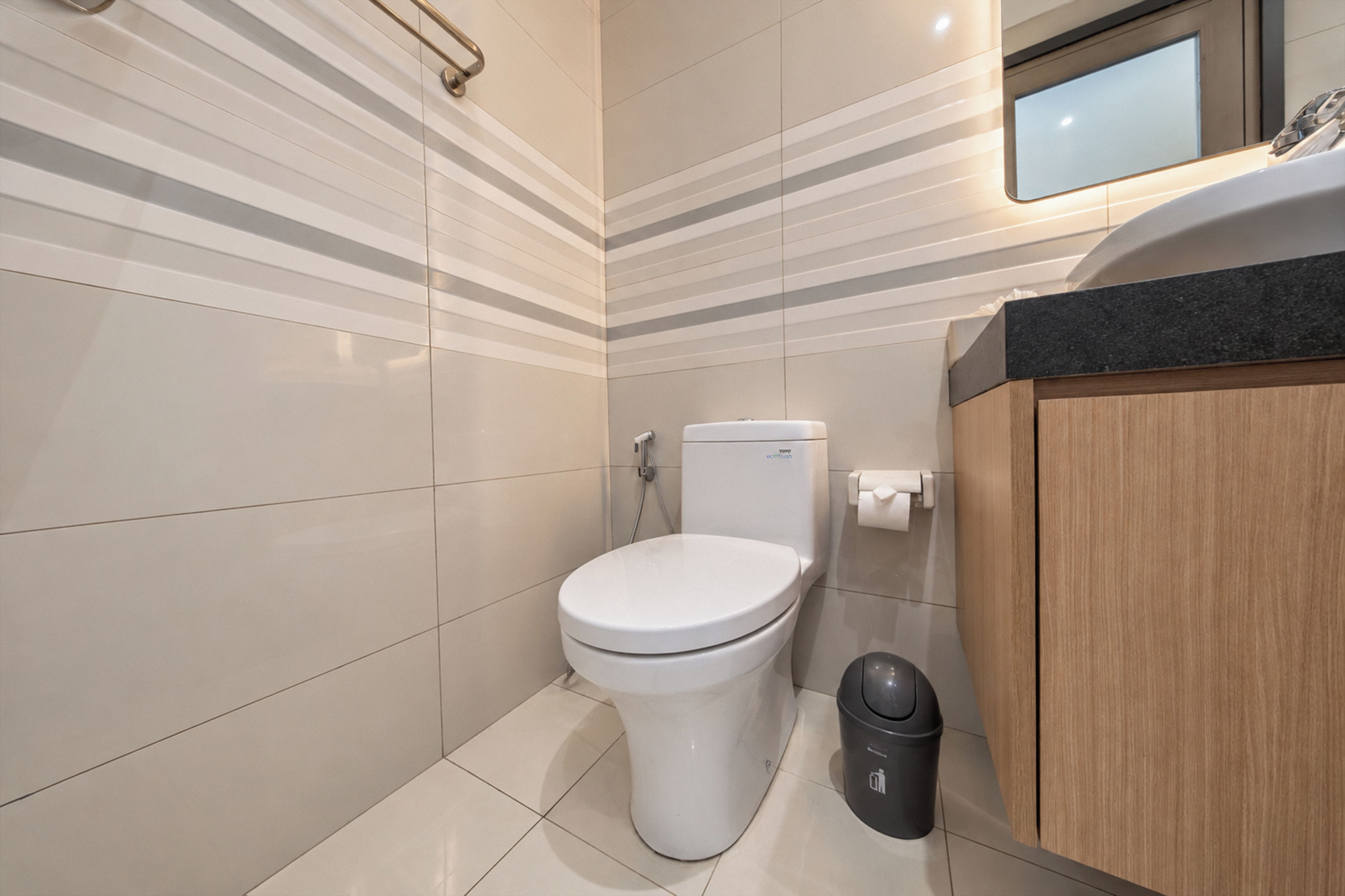 Un baño moderno con inodoro, un cubo de basura y un armario de madera.