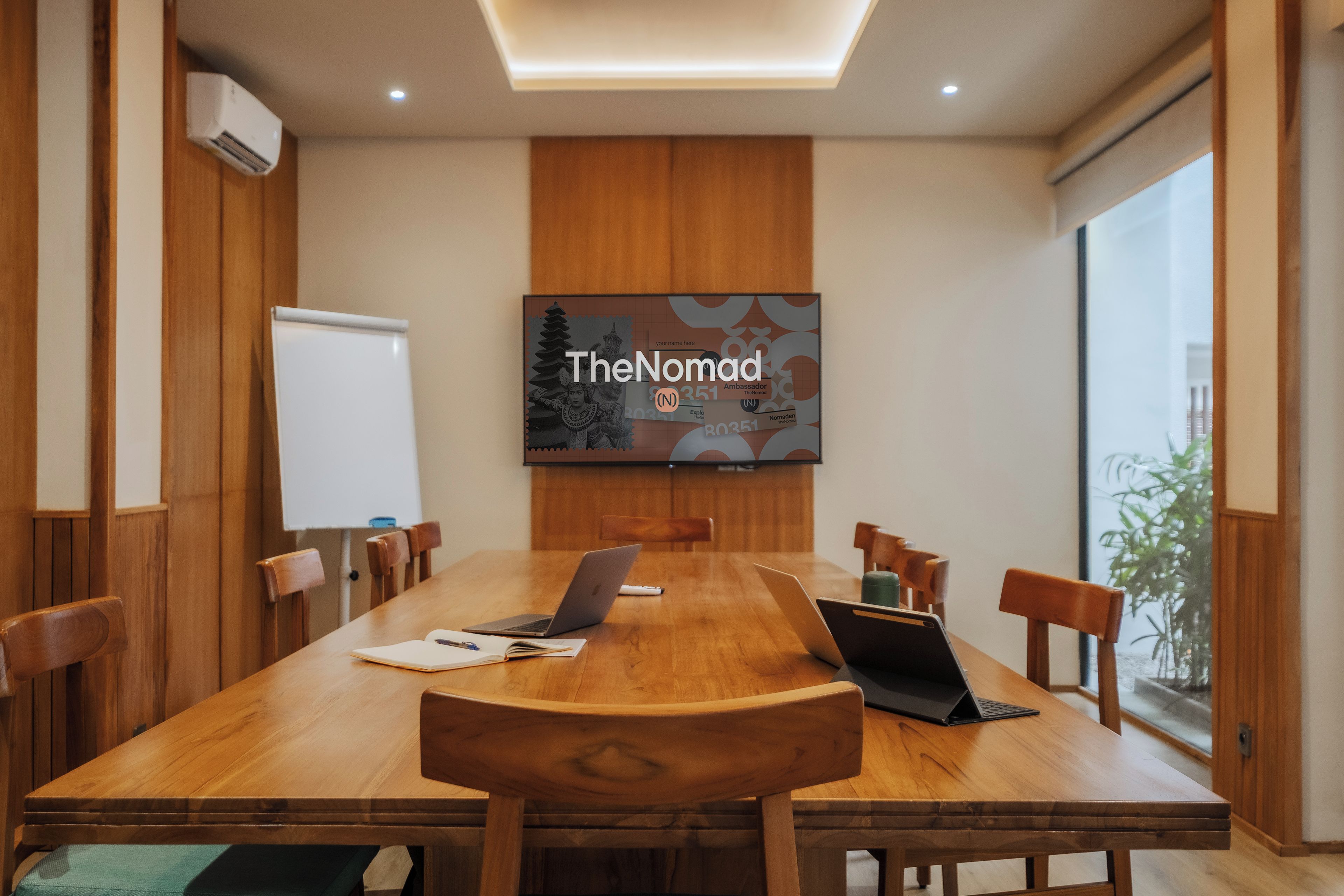 A conference room with a large table, chairs, laptops, and a TV screen displaying 'TheNomad'.