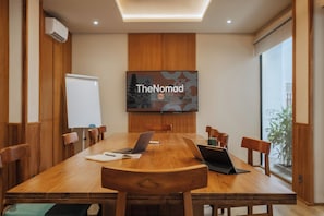 A conference room with a large table, chairs, laptops, and a TV screen displaying 'TheNomad'. - TheNomad Canggu (Canggu)