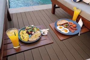 A breakfast setup on a wooden deck with a pool in the background. - TheNomad Canggu (Canggu)