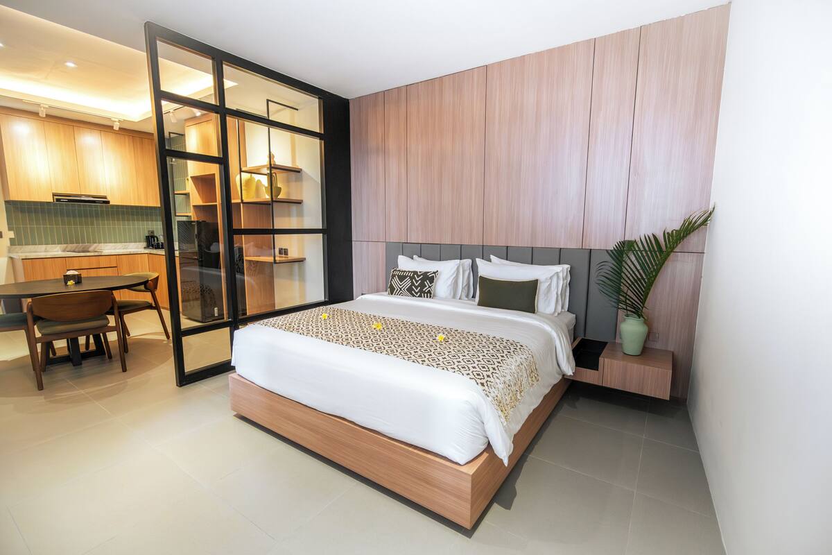 A modern hotel room with a bed, a desk, and a kitchenette.