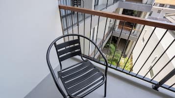 A black metal chair on a balcony with a metal railing and a view of buildings and greenery below.