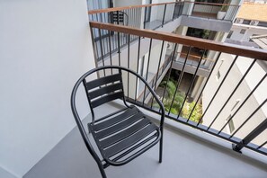 A black metal chair on a balcony with a metal railing and a view of buildings and greenery below. - TheNomad Canggu (Canggu)