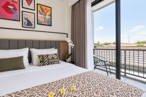 A hotel room with a bed, a balcony with a view, and a wall with framed pictures. - TheNomad Canggu (Canggu)