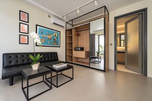 Un salon moderne avec un canapé noir, une table basse et une plante en pot. Un tableau encadré orne le mur, et une grande fenêtre laisse entrer la lumière naturelle.