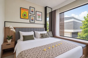 A hotel room with a large bed, a nightstand, a potted plant, and a window with a view of a building and trees.