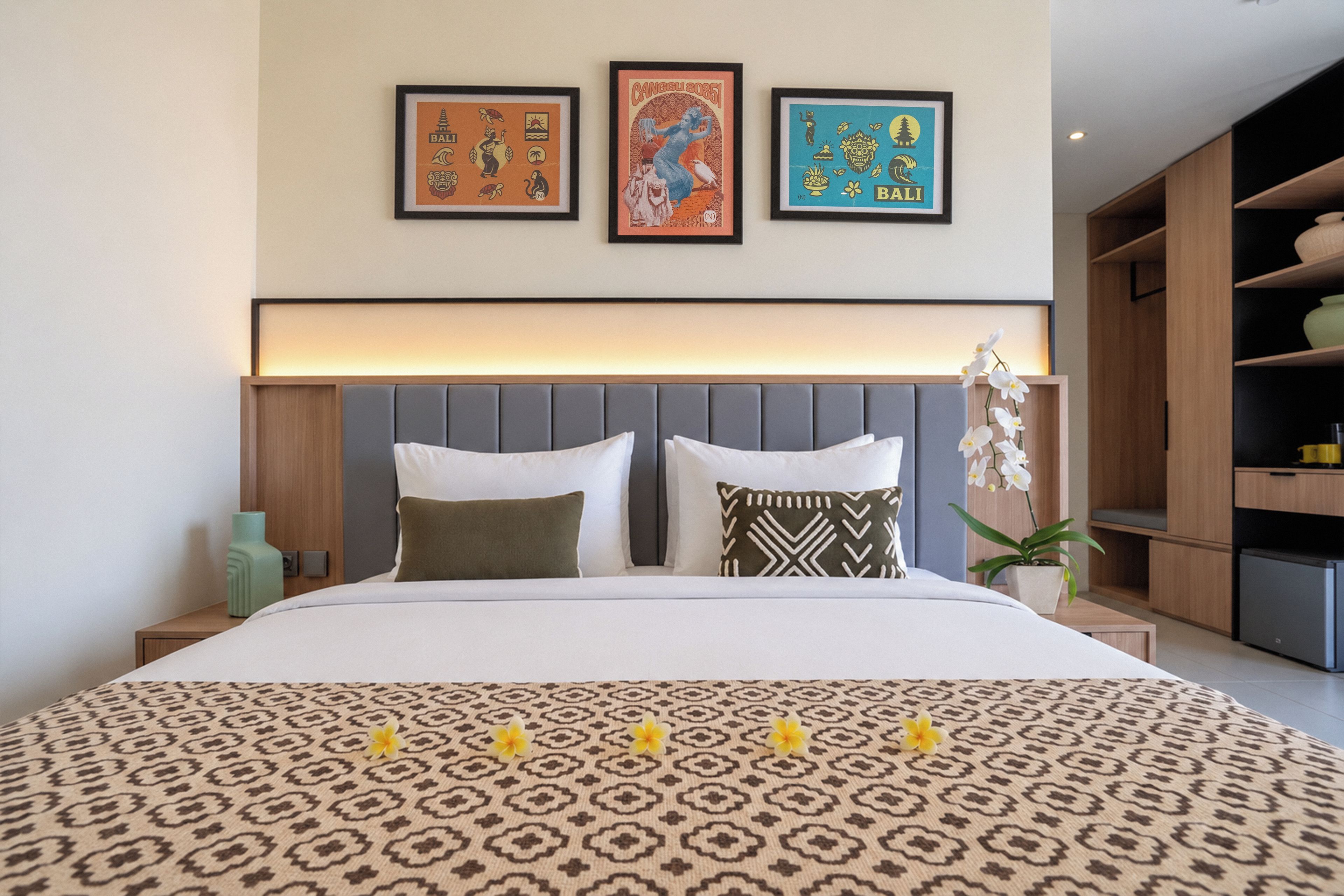 A hotel room with a bed, a nightstand, a wall-mounted shelf, and three framed pictures above the bed.