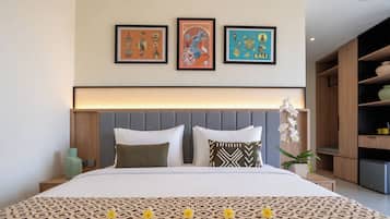 A hotel room with a bed, a nightstand, a wall-mounted shelf, and three framed pictures above the bed.
