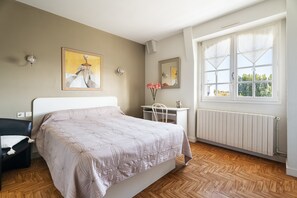 Une chambre à coucher comprenant un lit, un bureau, une chaise, un radiateur et une fenêtre donnant sur un paysage agréable.