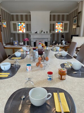 A dining table set with various utensils, a bottle of syrup, and a jar of jam.