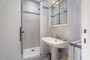 Un baño moderno con ducha de vidrio, lavabo blanco y un espejo grande.