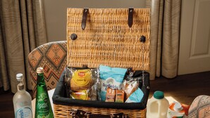 Una cesta de mimbre llena de alimentos y bebidas sobre una mesa de madera.