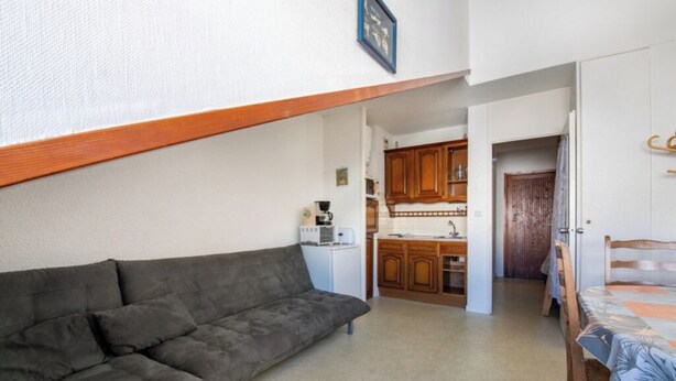 Un espacio habitable compacto con sofá, una mesa de comedor con sillas y una kitchenette.