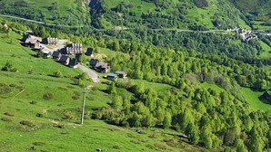 Un paisaje rural con un pequeño grupo de casas en una ladera, rodeado de exuberante vegetación y montañas al fondo.