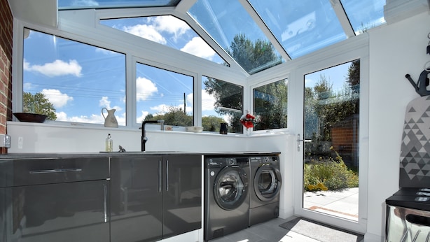 A modern kitchen with a built-in washer and dryer, large windows, and a skylight.