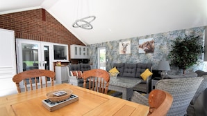 A spacious living area with a dining table, grey sofas, and a brick wall.